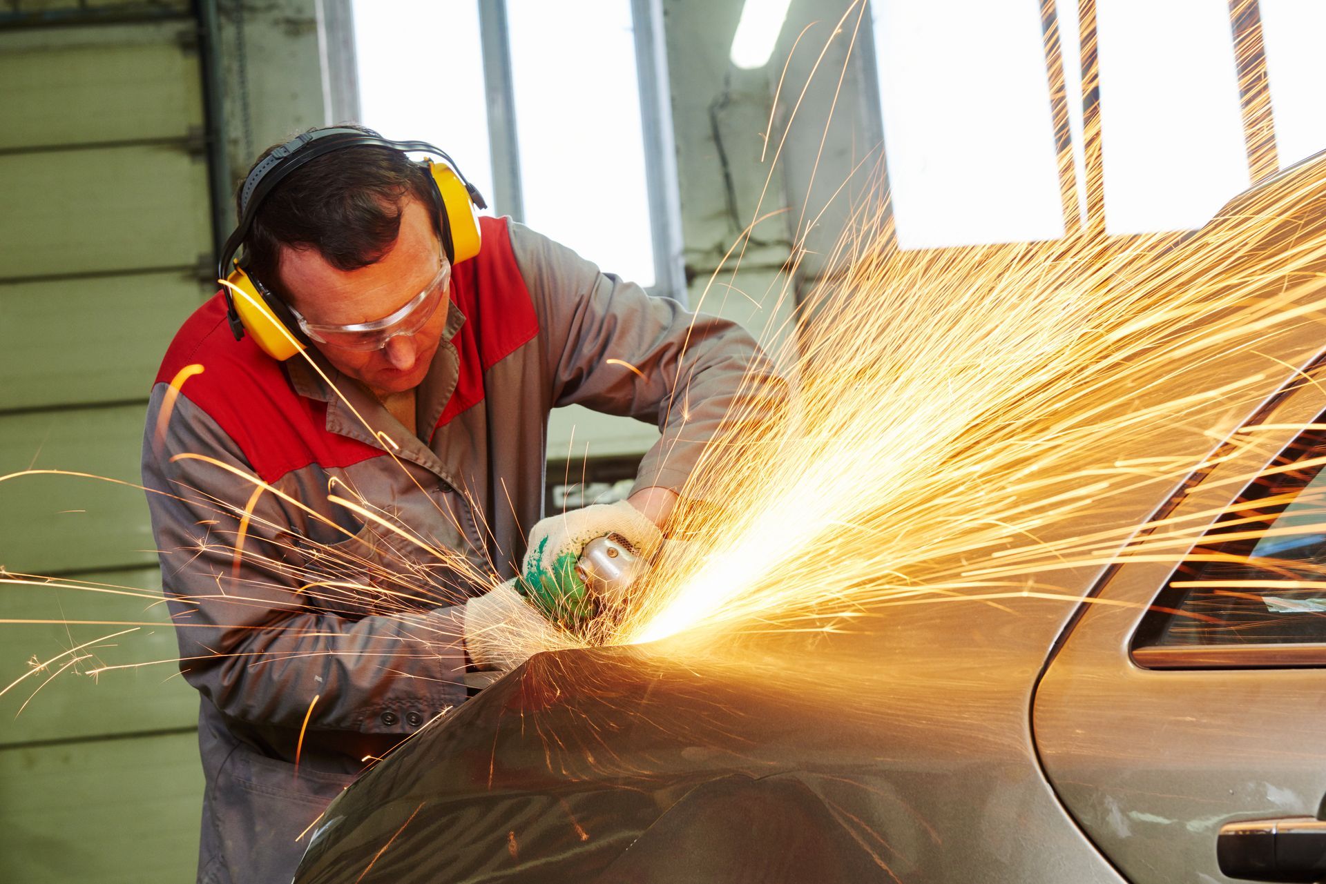 Auto mechanic using an angle grinder on a car in a repair shop.