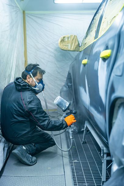 Person spray-painting a car body in a masked auto shop booth