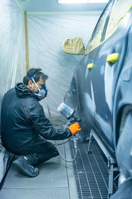 Person spray-painting a car body in a masked auto shop booth