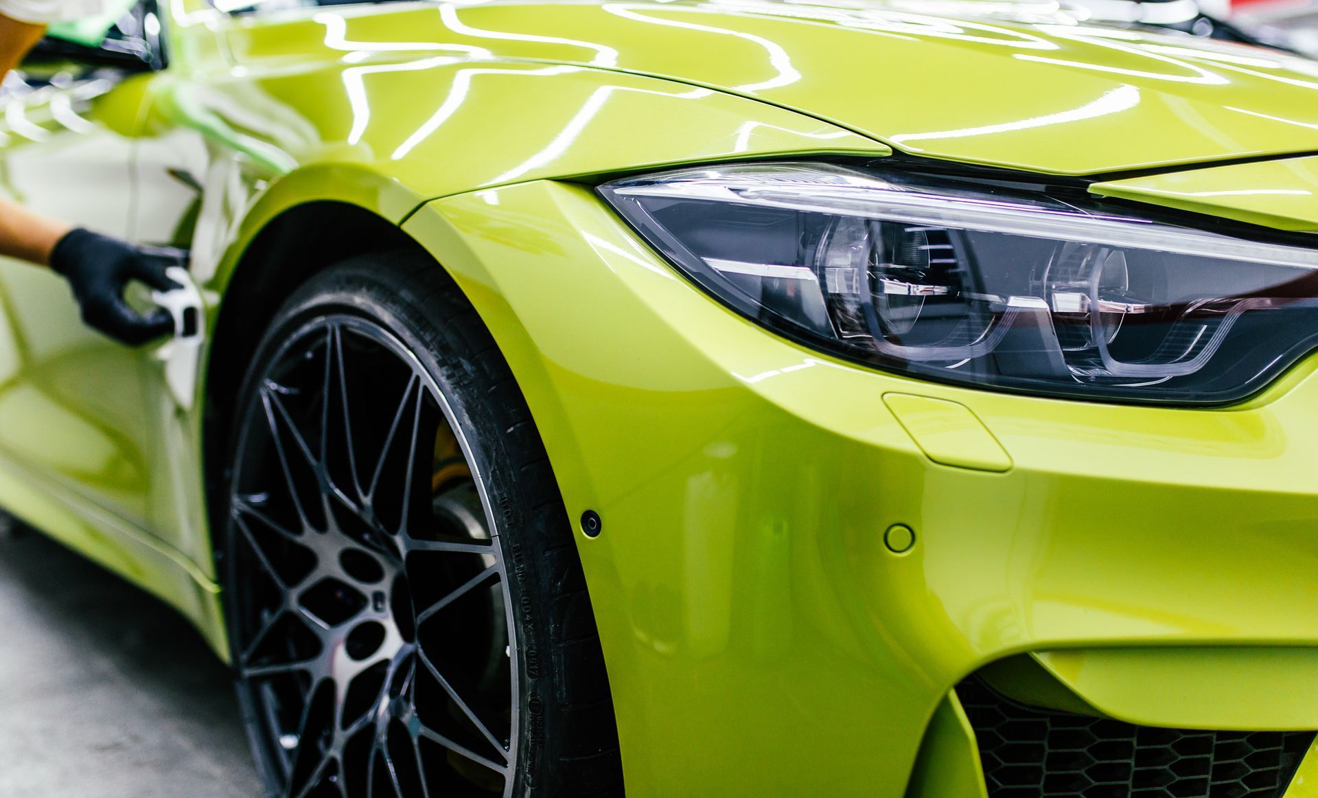Close-up of a lime green sports car’s front wheel and headlight being washed in a garage