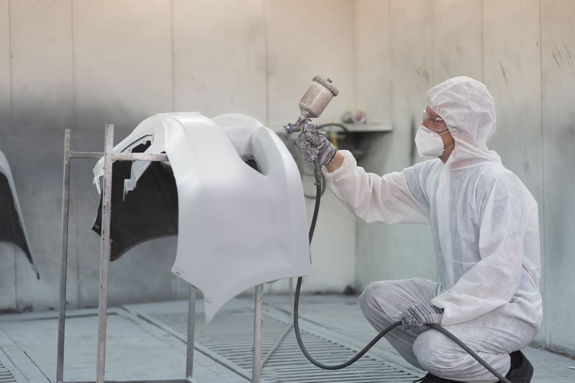 Worker in white protective gear spray-painting a car body in a paint booth.