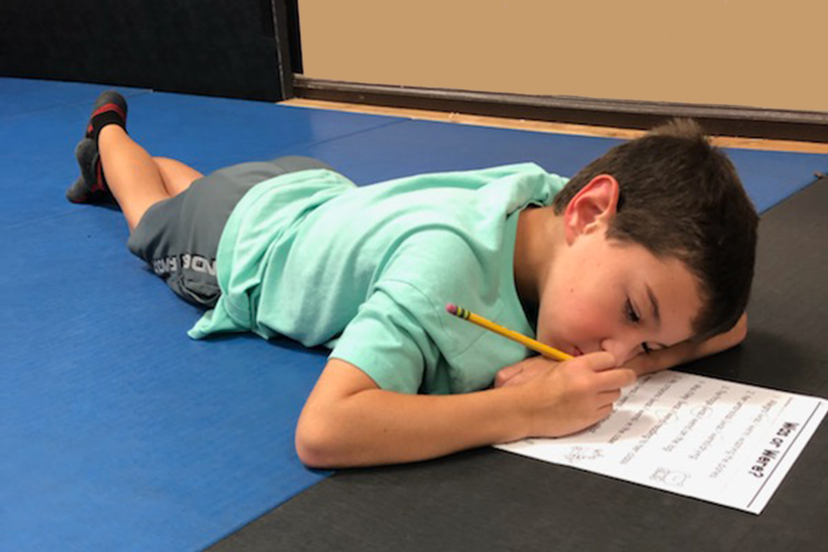 A young boy is laying on the floor writing on a piece of paper.