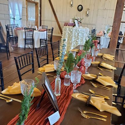 A long table with plates , utensils , napkins and flowers on it.