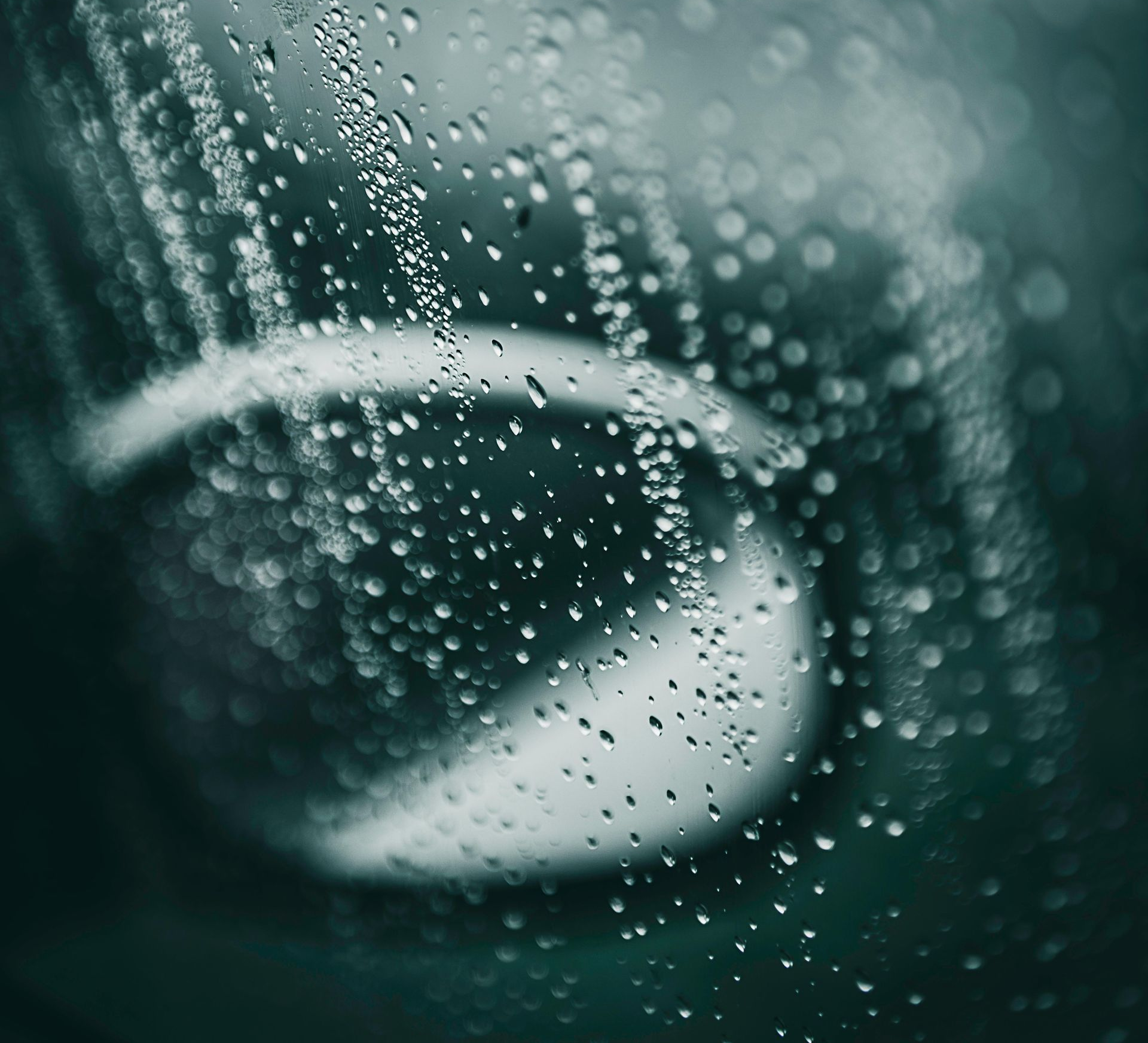 Raindrops on a car window obscuring the side mirror, creating a blurred, watery view.