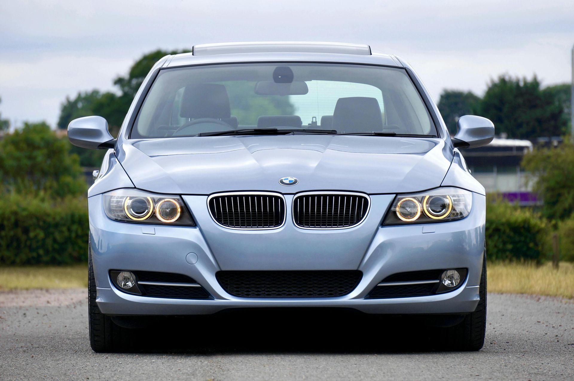 Light blue BMW sedan, front view, outdoors on asphalt.