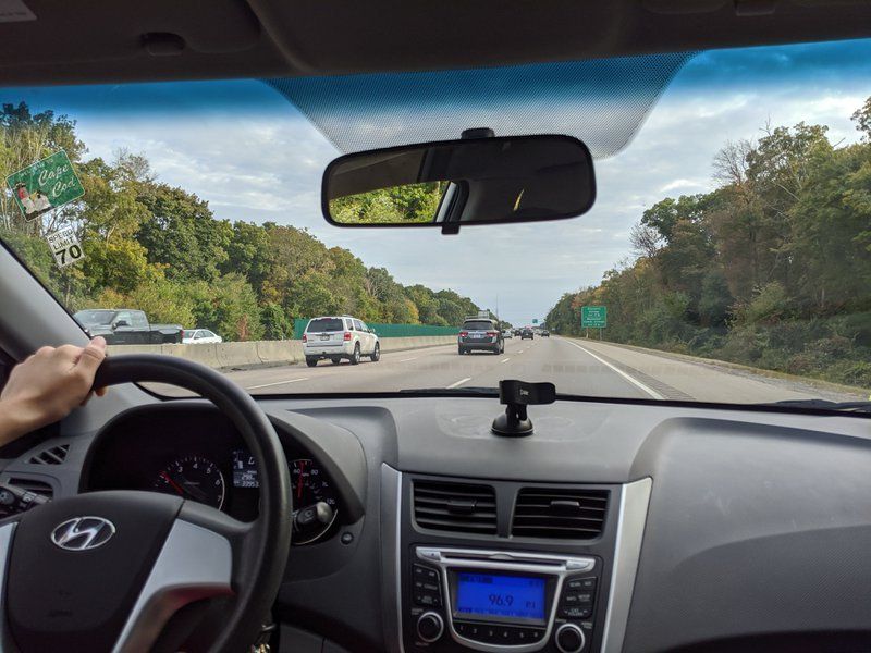 Raindrops on a window obscure a blurry, dark interior, possibly a car's dashboard.