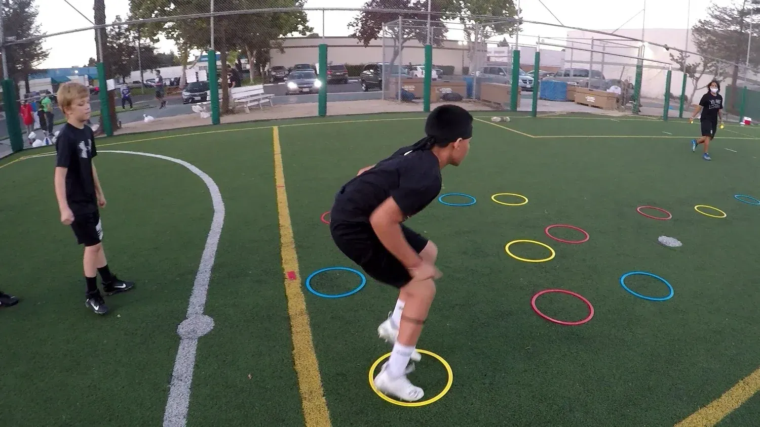 Boy jumping through yellow agility rings on a green field. Others watch.