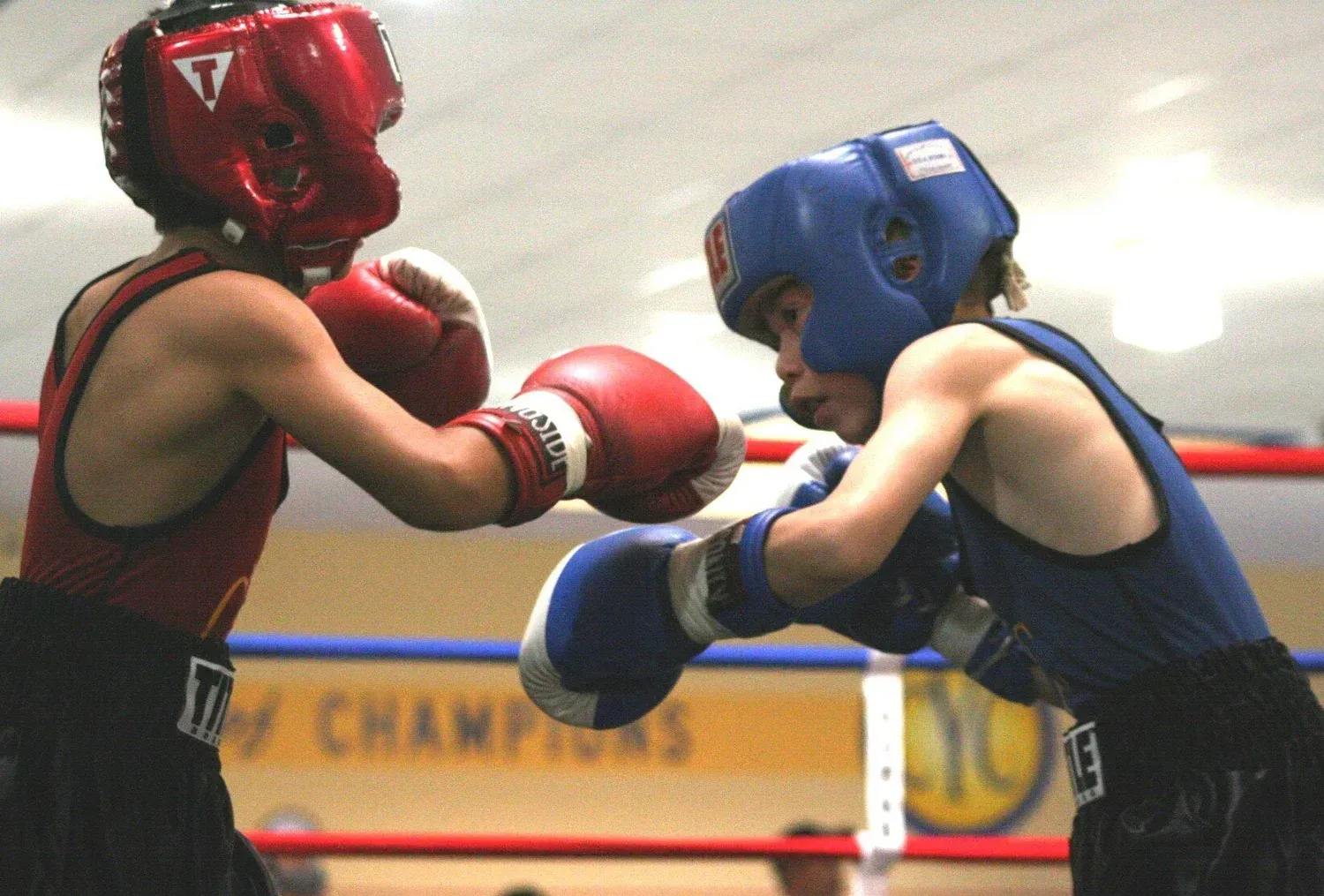 Two young boxers sparring in a ring, wearing headgear, gloves, and athletic attire.