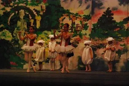 Ballet dancers in white tutus and sheep costumes on stage with a painted backdrop.