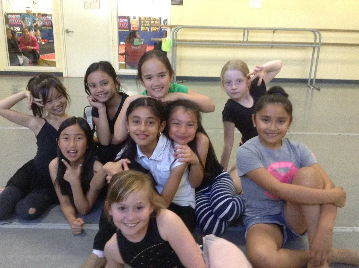 Group of young dancers in a studio, smiling, posing in various stances.
