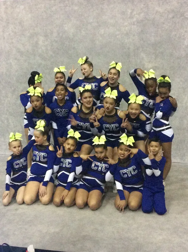 Cheerleading team in blue and white uniforms with neon yellow bows, posing against a gray backdrop.