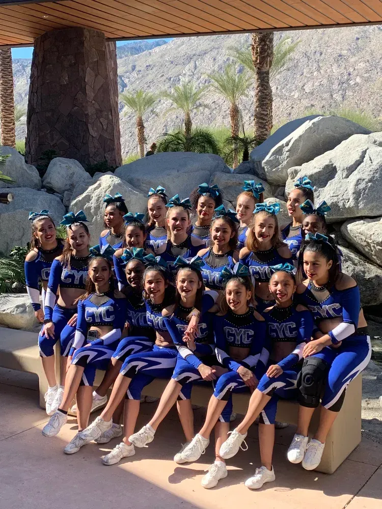 Cheerleading team in blue and white uniforms poses outdoors, mountains in the background.