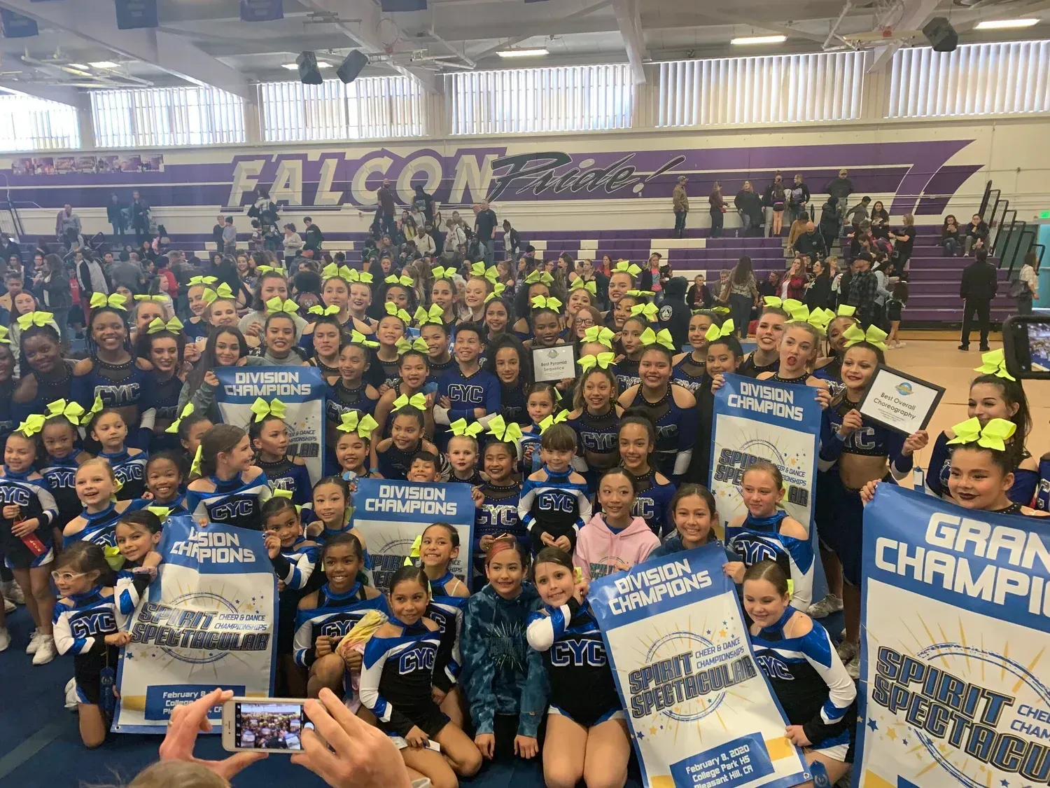 Cheerleaders in blue, white, and black uniforms holding banners, posing in a gym with