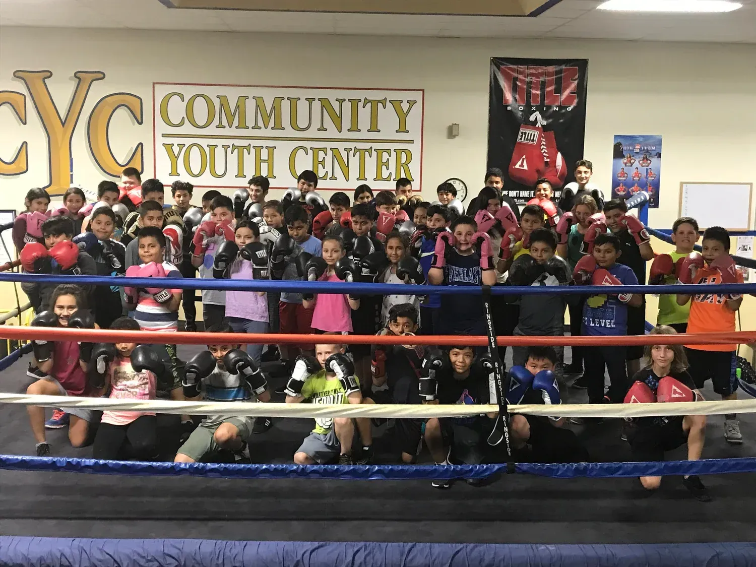 A large group of children with boxing gloves in a boxing ring at the Community Youth Center.