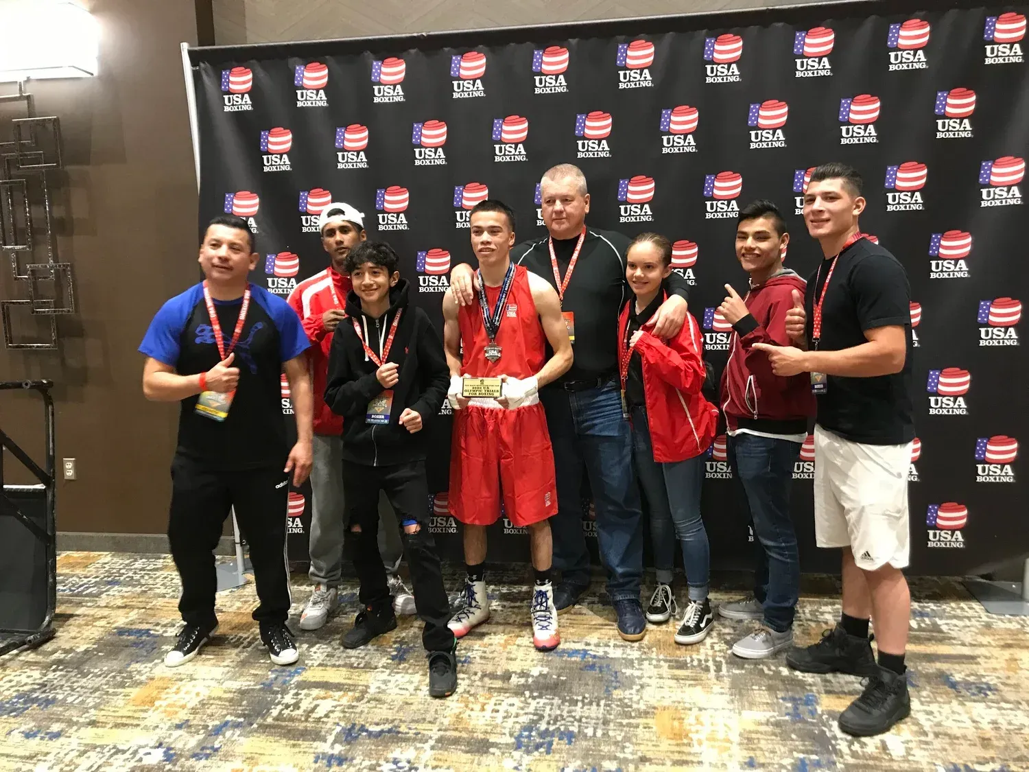 Group poses in front of a backdrop, celebrating a boxer wearing red trunks and a medal.