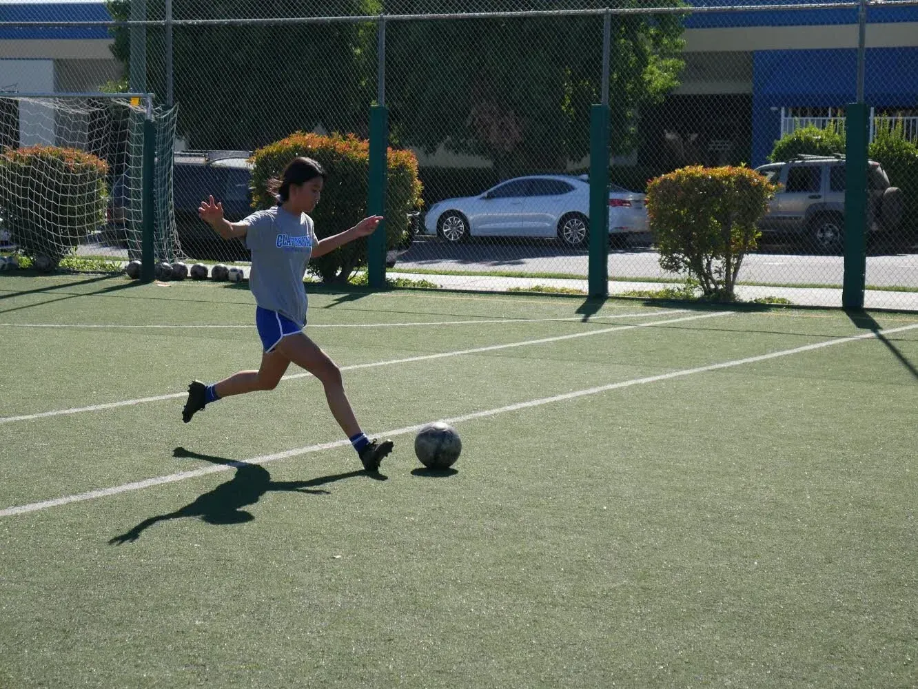 Person kicking a soccer ball on a green turf field, sunny day.