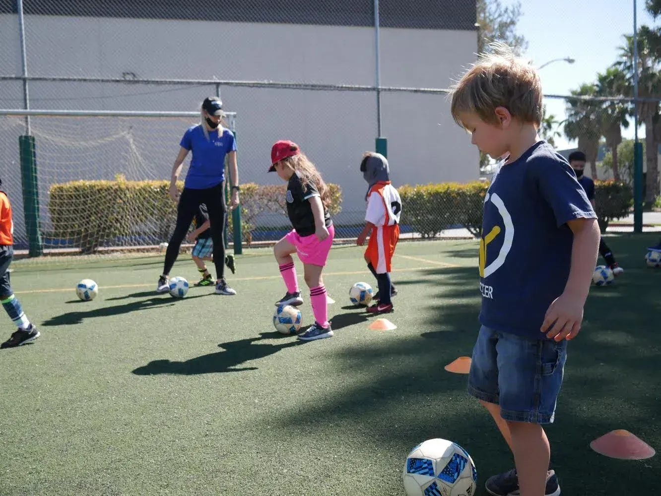 Children practicing soccer skills with an instructor on a green field.