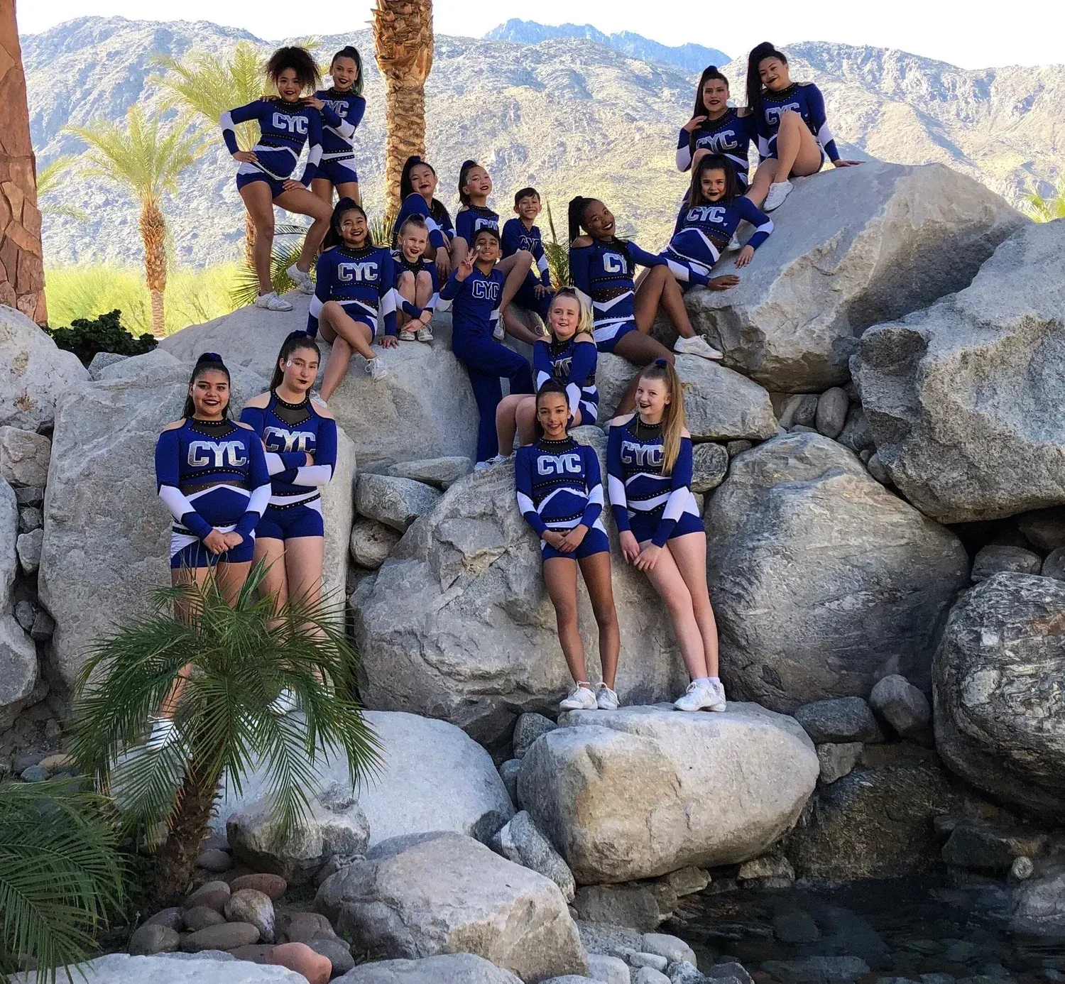 Cheerleading team in blue CYC uniforms poses on rocks; mountains in background.