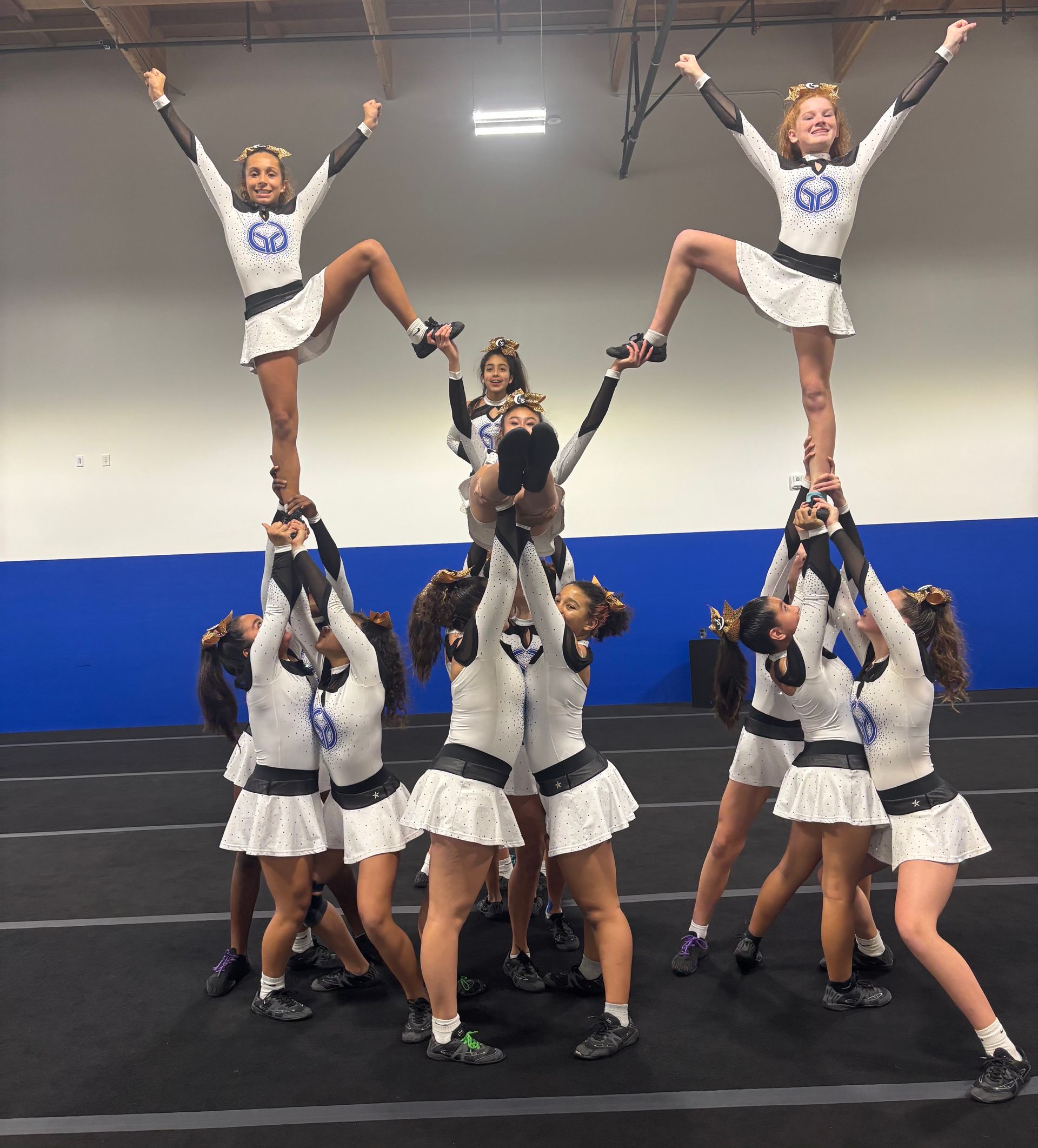 Cheerleaders in blue and white uniforms perform a stunt on a grassy field with palm trees.