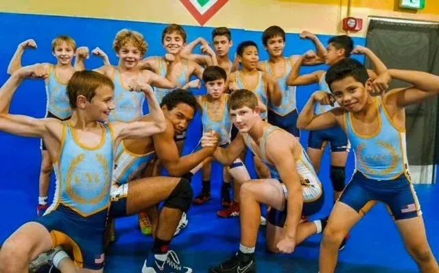 Youth wrestling team flexing in blue and gold uniforms on a blue mat.