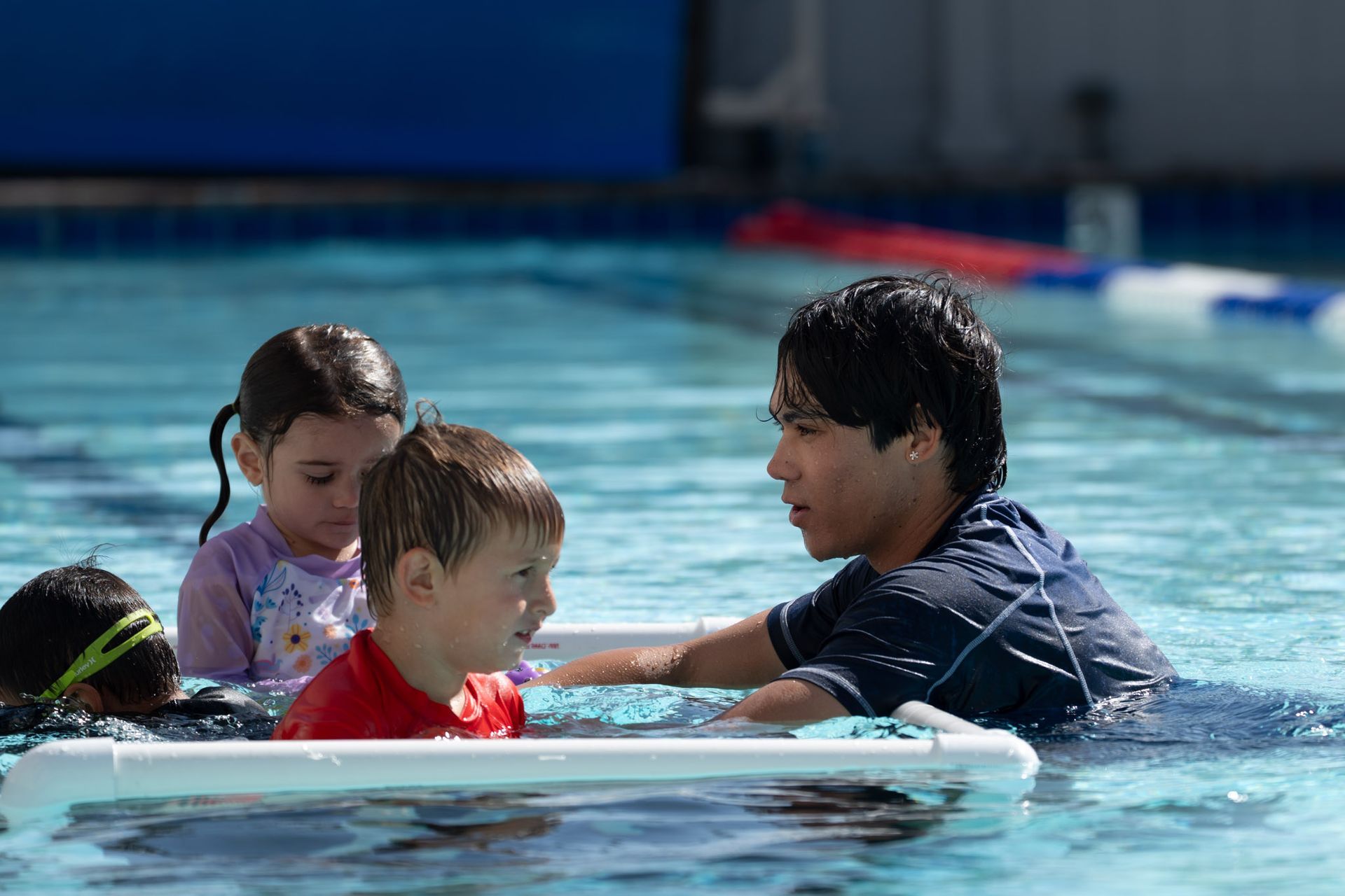 Children in a swimming pool with an instructor, holding a float board during a lesson