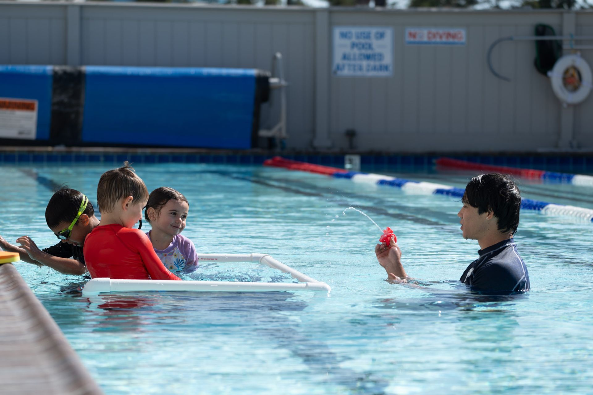 People in a swimming pool with an instructor holding a red toy