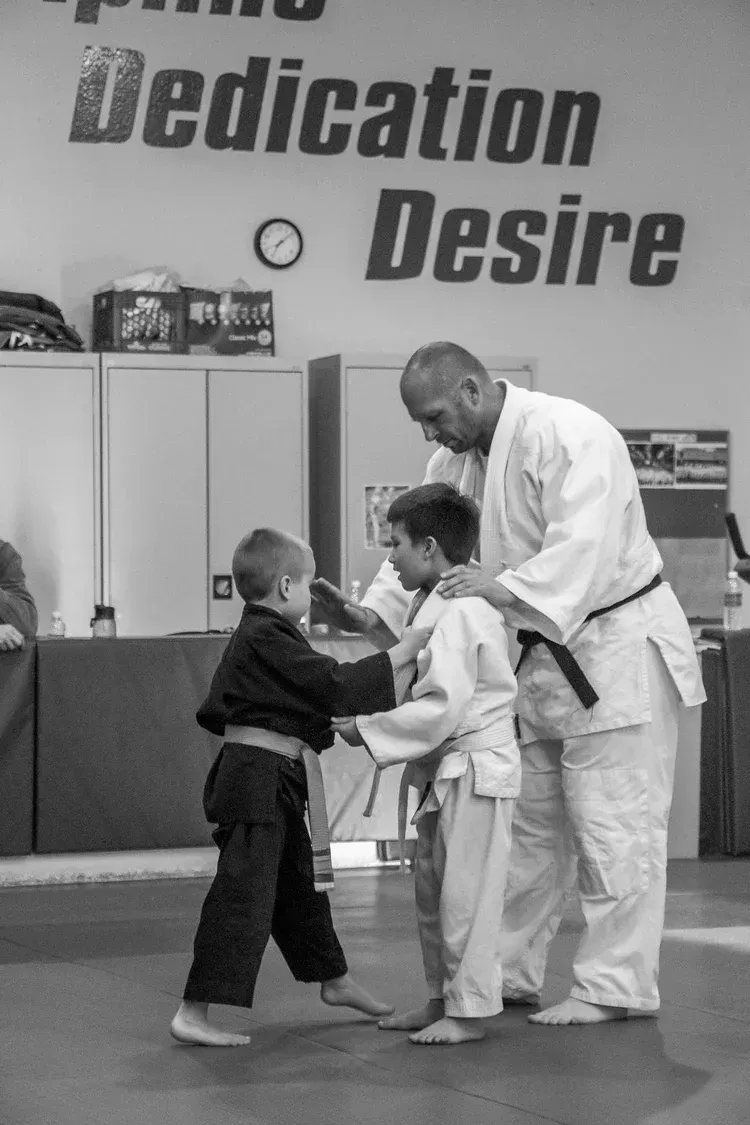 Instructor guiding two young students in martial arts practice.