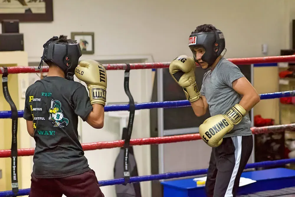 Two boxers sparring in a ring, wearing headgear and gloves.