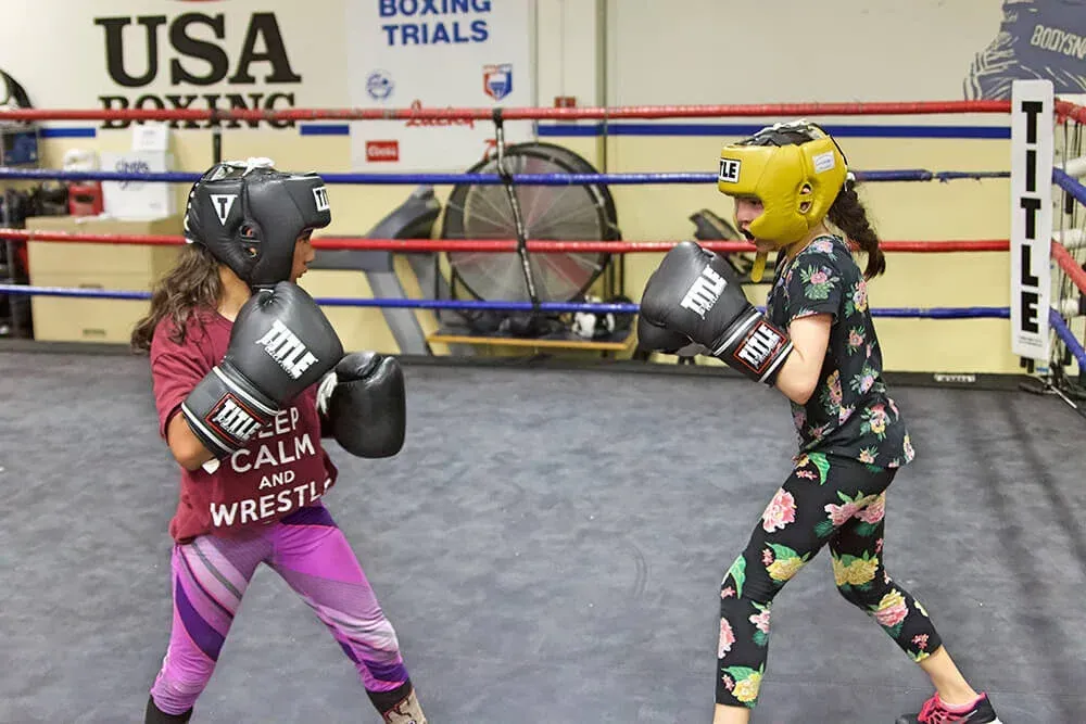 Two young boxers wearing headgear and gloves sparring in a boxing ring.