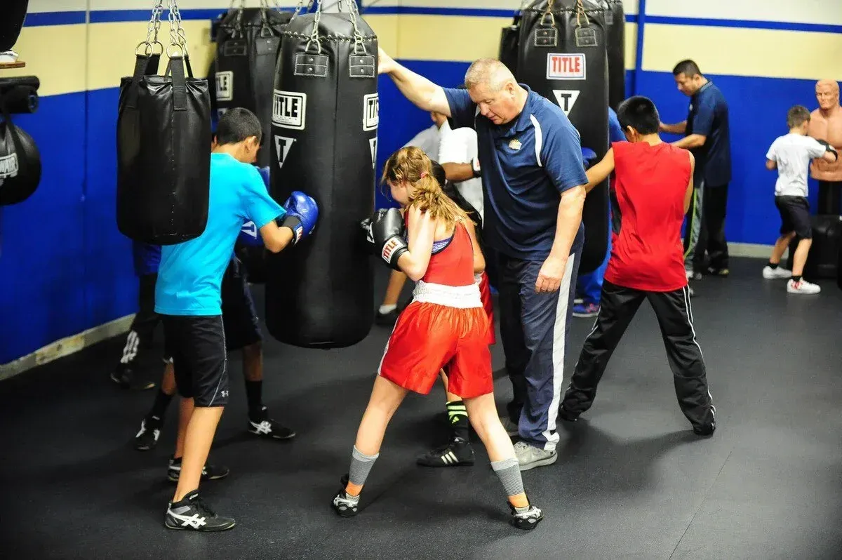 Boxing class: Instructor guides students practicing punches on heavy bags in a gym.