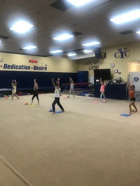 Gymnasts in a gym exercising with their arms raised. White, tan, and blue interior.
