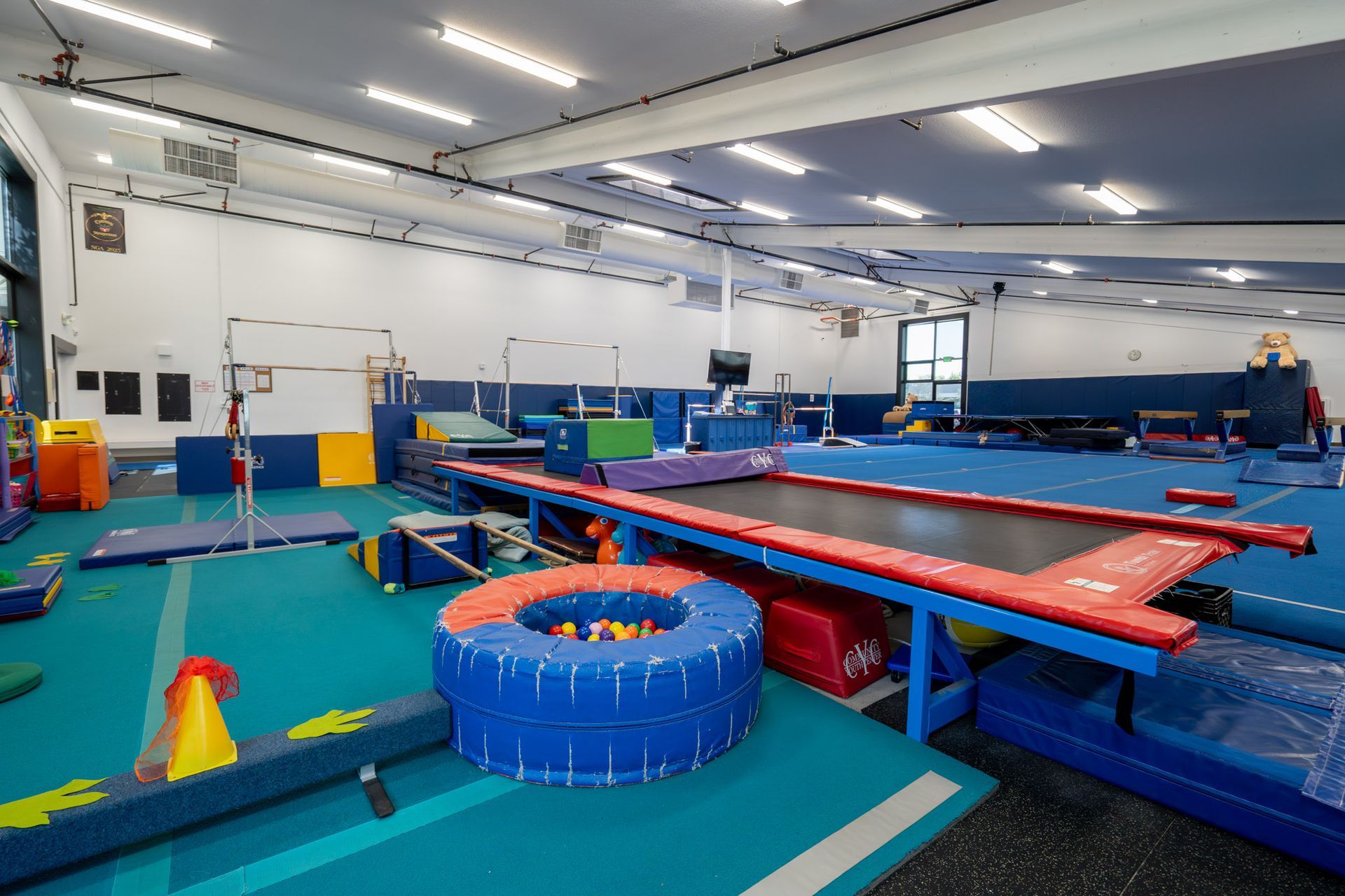 Indoor gymnastics training area with blue mats, trampolines, foam pits, and balancing equipment