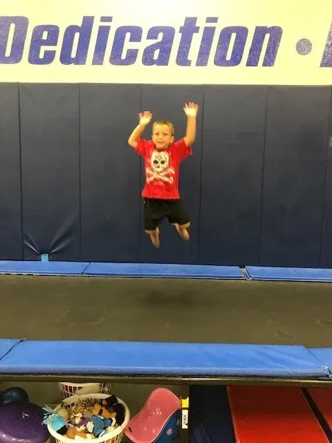 Boy jumping on a trampoline, arms raised, against a blue wall with the word