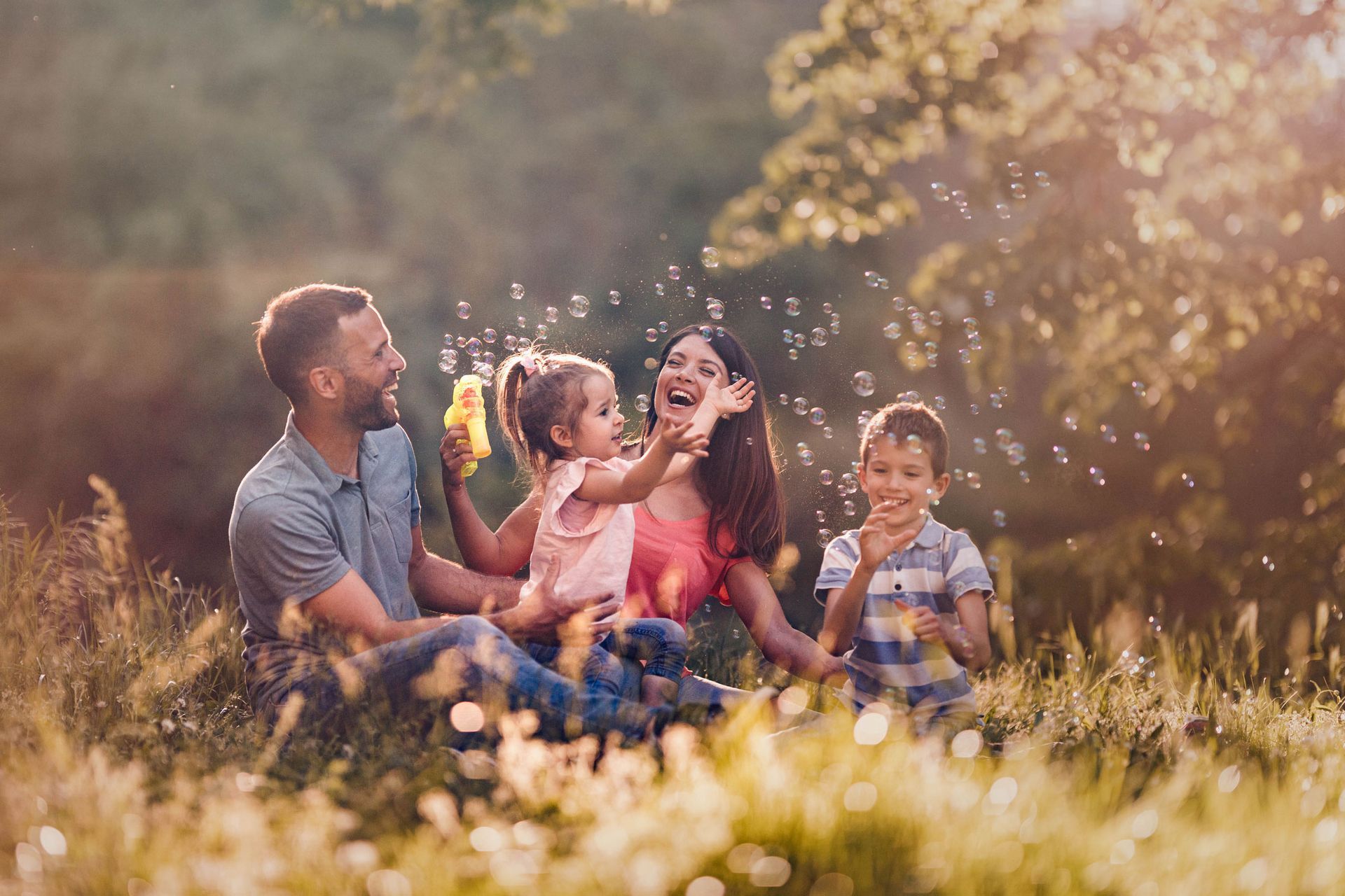 Family playing with bubbles in a sunlit grassy field, smiling.