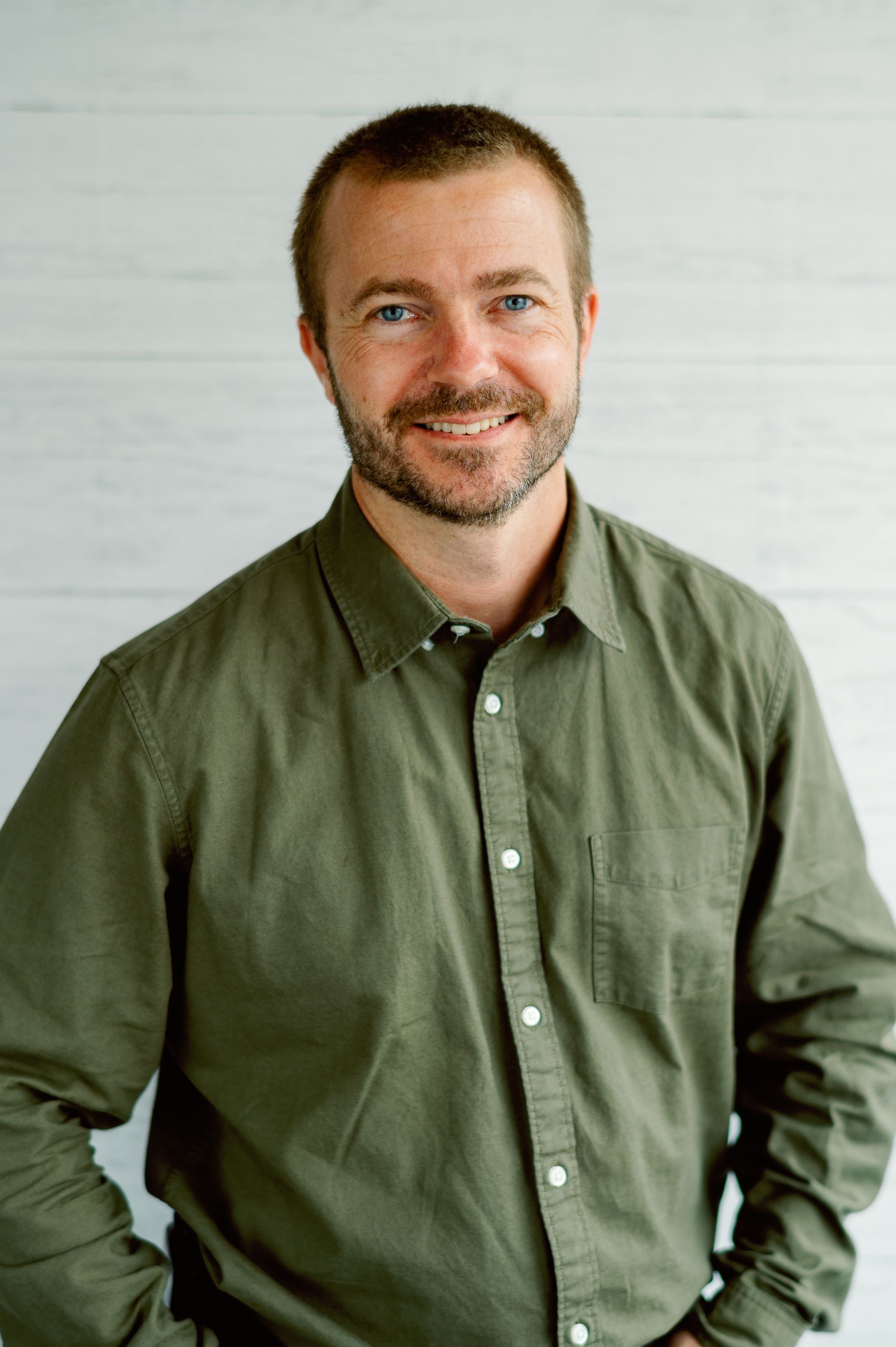 A man with a beard is wearing a green shirt and smiling.