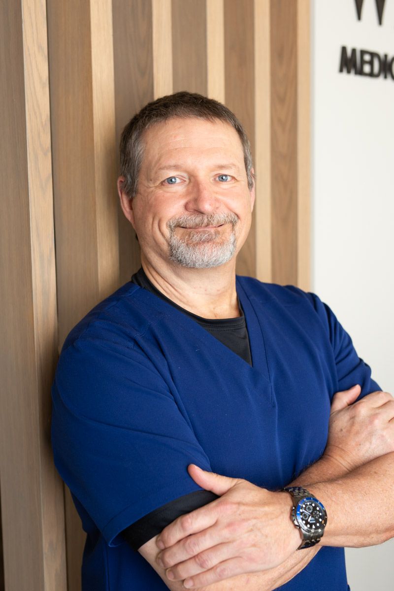 A man in a blue scrub is standing with his arms crossed