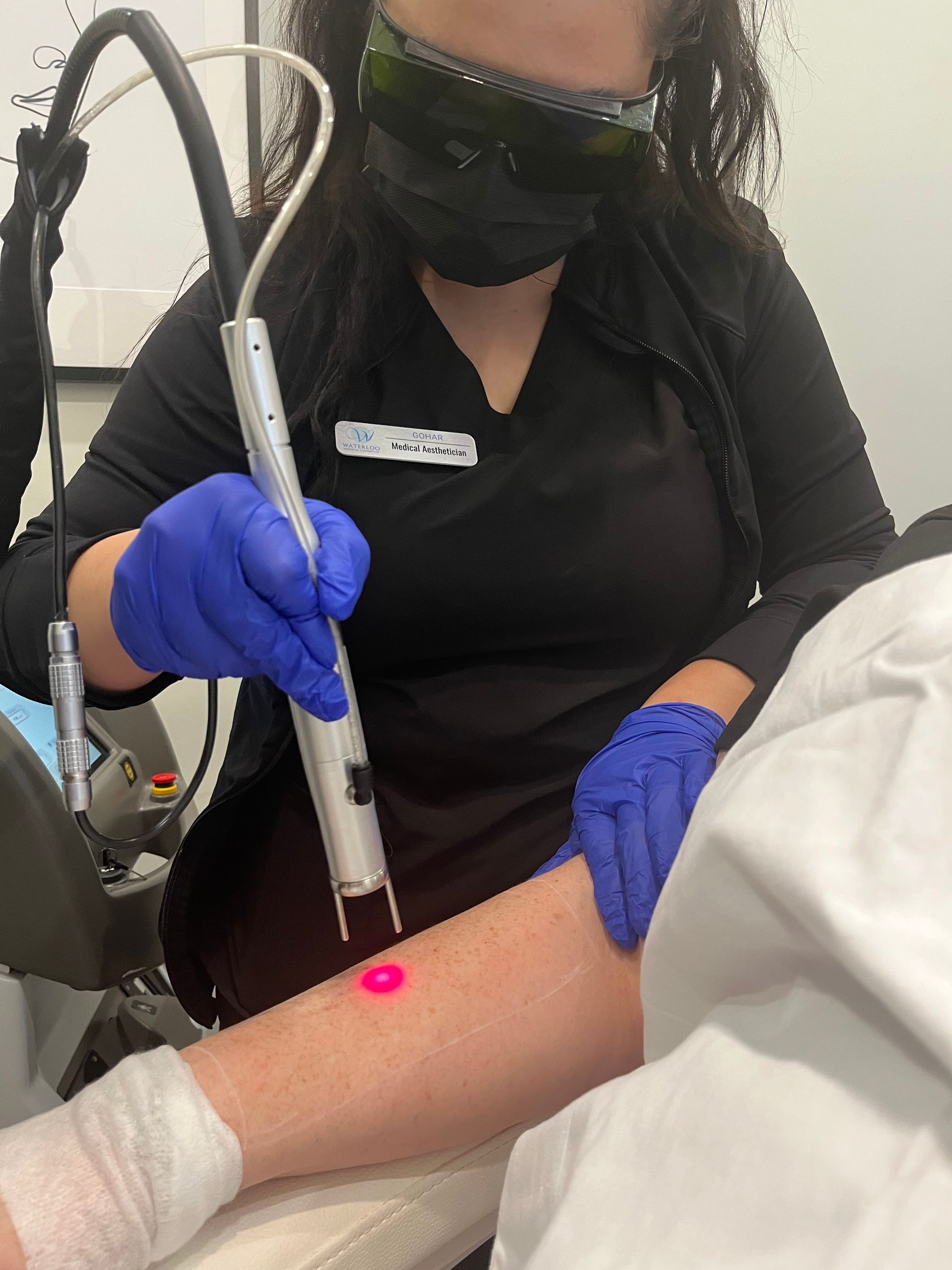 A woman wearing a mask and gloves is using a laser on a patient 's arm.