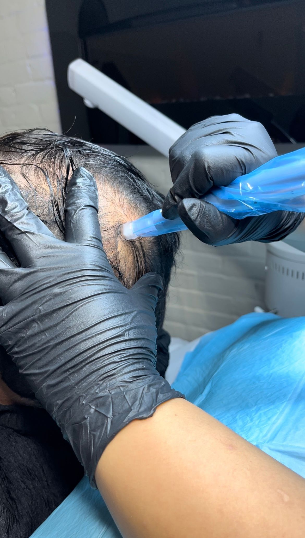 A person wearing black gloves is getting a hair treatment.