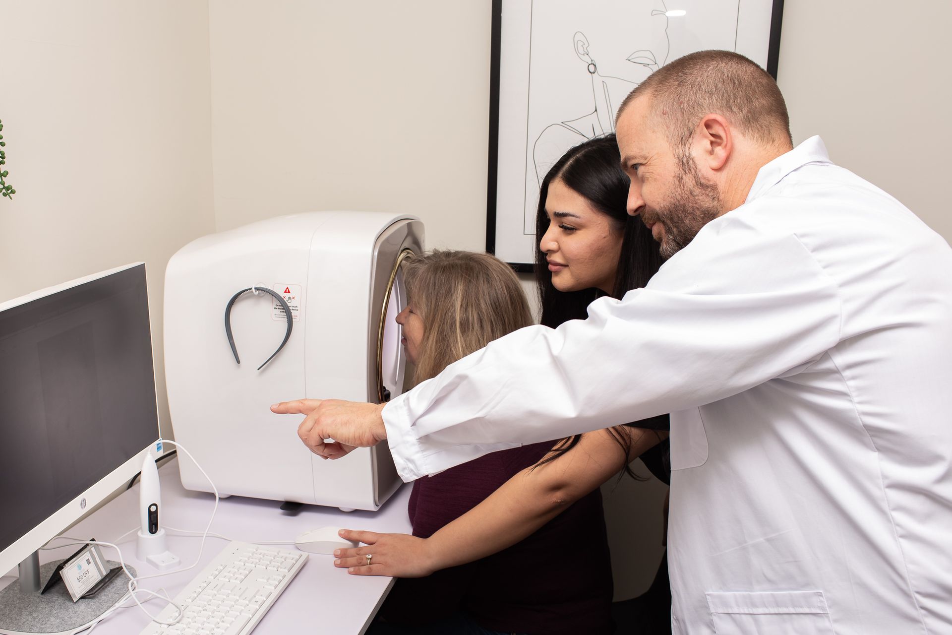 A man in a lab coat is pointing at a machine while a woman looks on.