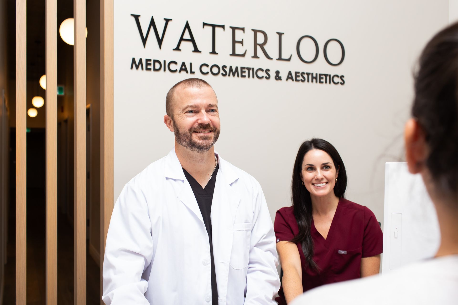 A man and a woman are standing in front of a sign that says waterloo medical cosmetics and aesthetics.