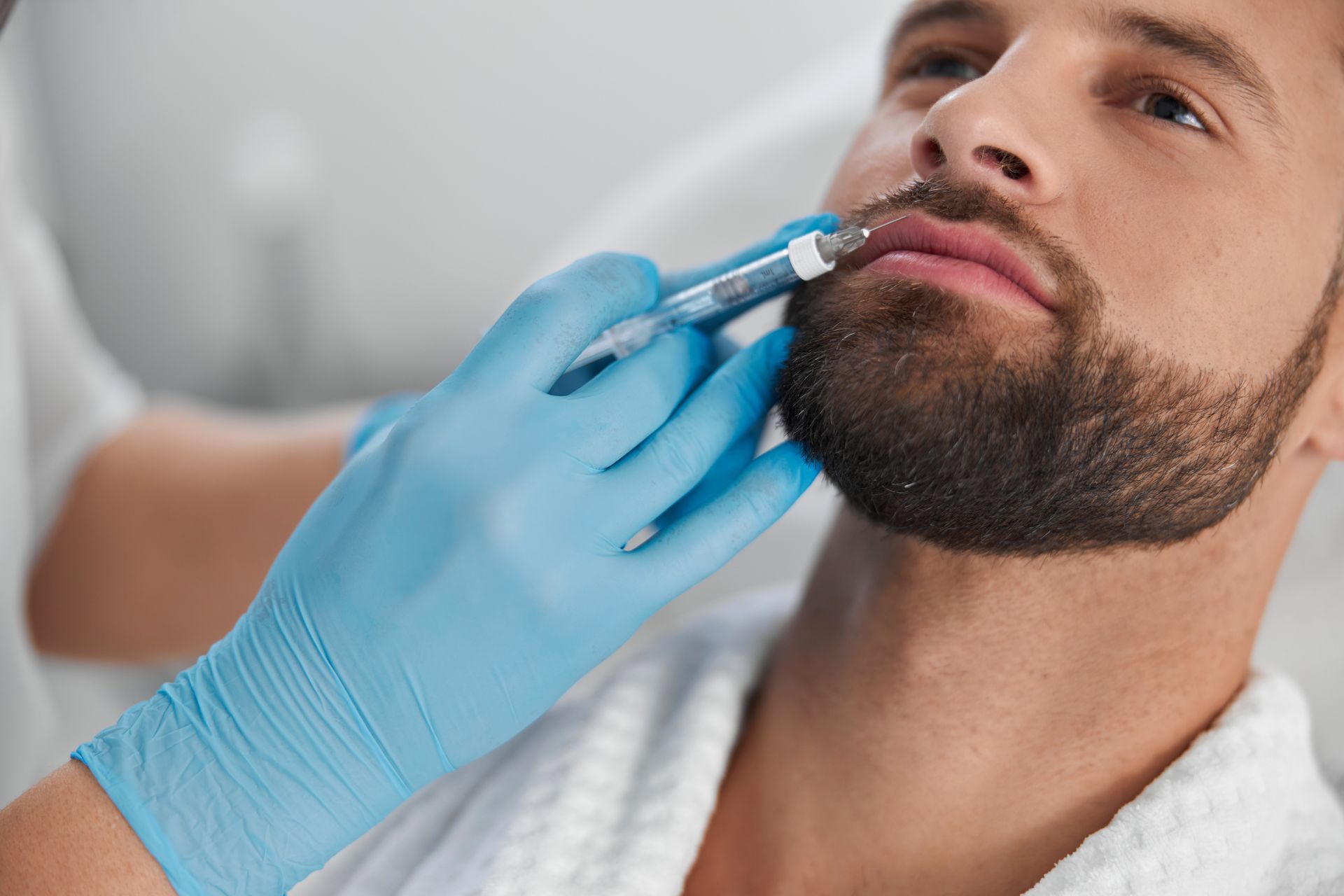 A man with a beard is getting a filler injection in his lips.