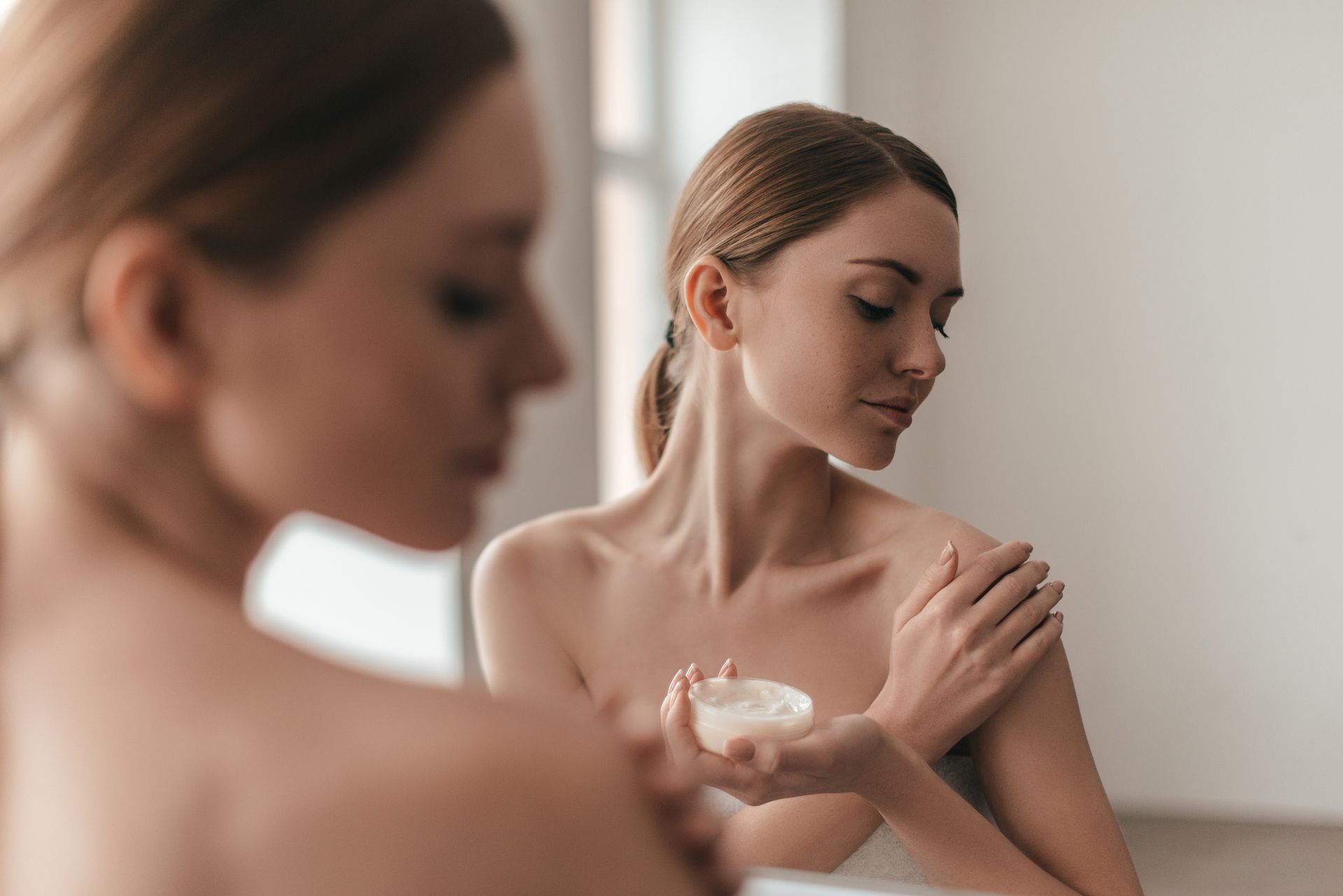 A woman is applying lotion to her shoulder in front of a mirror.