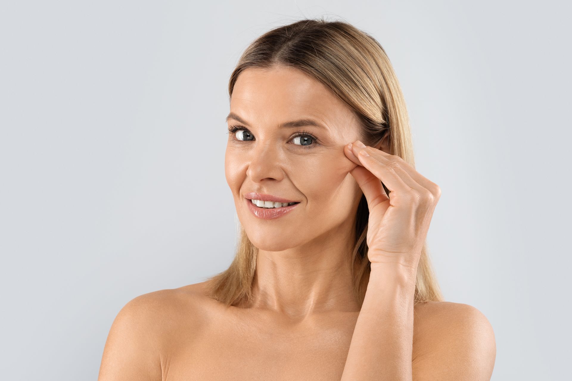 A woman is touching her face with her hand and smiling.