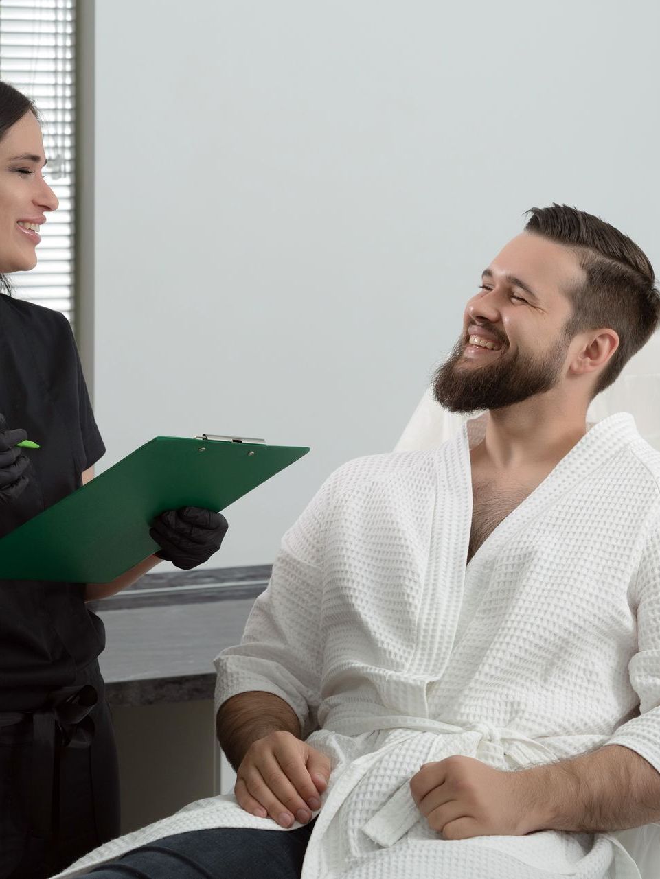 A man in a bathrobe is sitting in a chair talking to a female doctor.