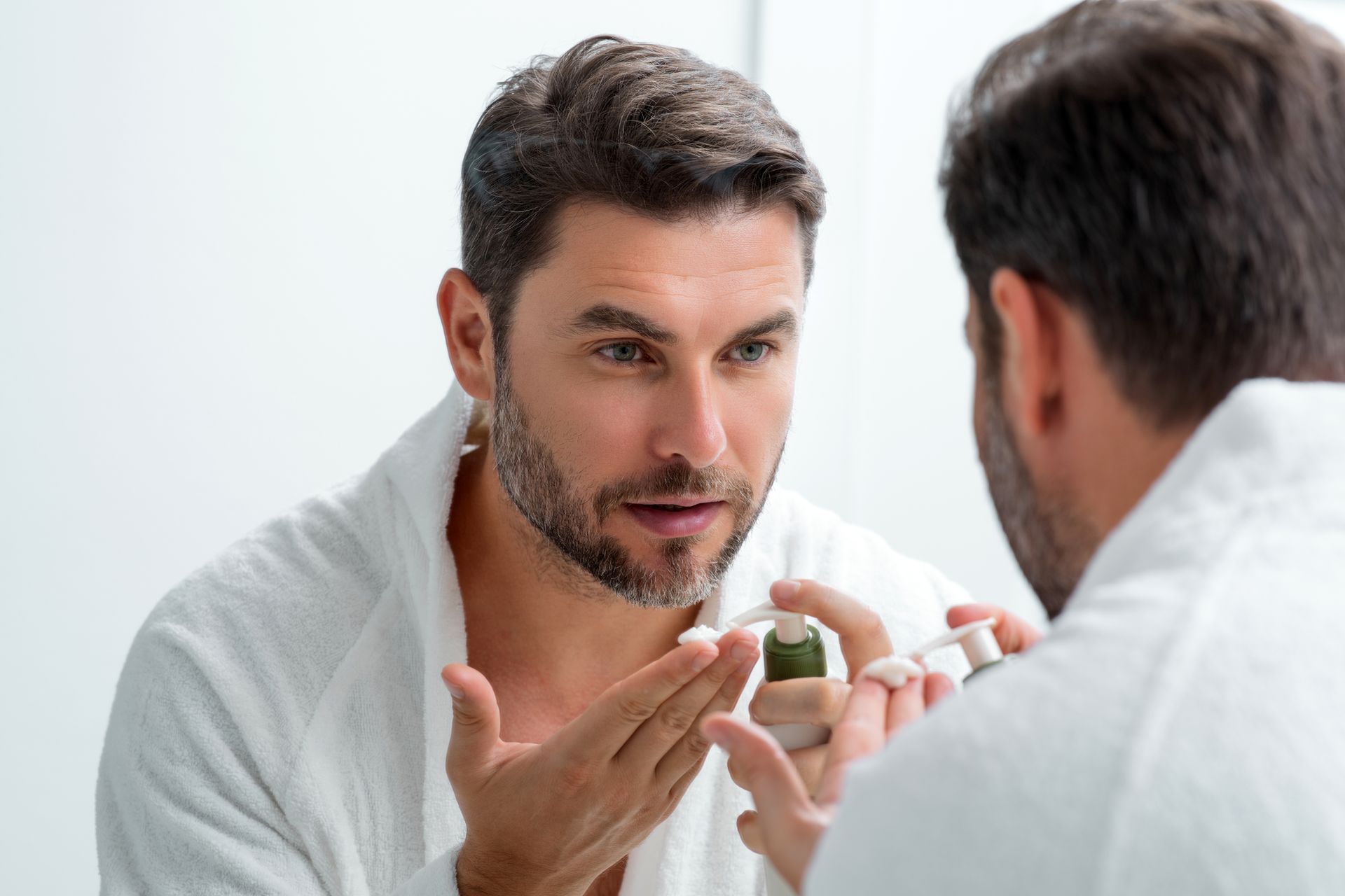 A man is applying lotion to his face in front of a mirror.