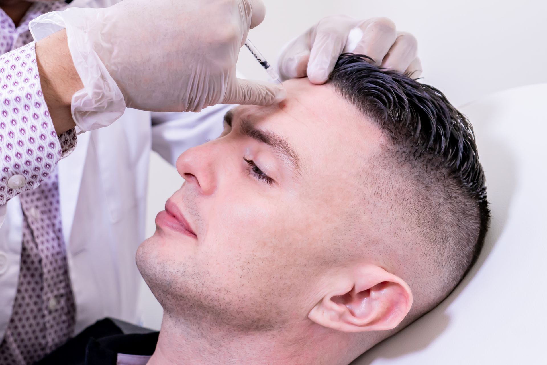 A man is getting an injection in his forehead by a doctor.