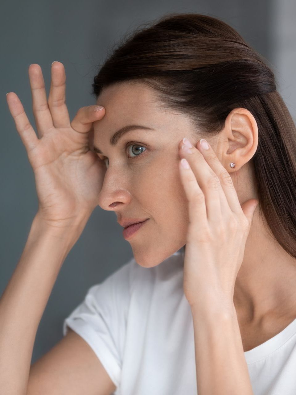 A woman is touching her face in front of a mirror.