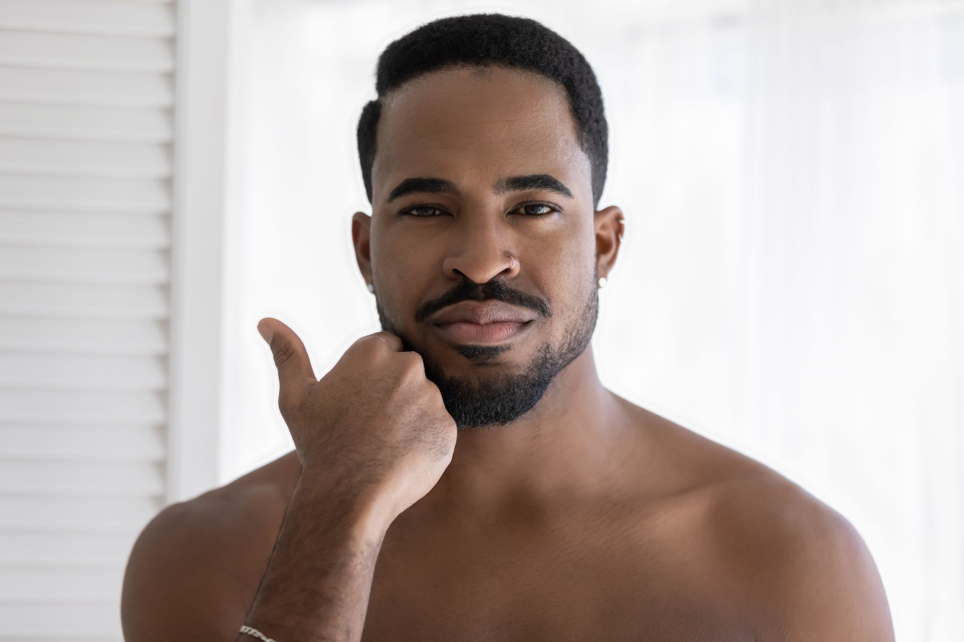 A shirtless man with a beard is looking at himself in the mirror.