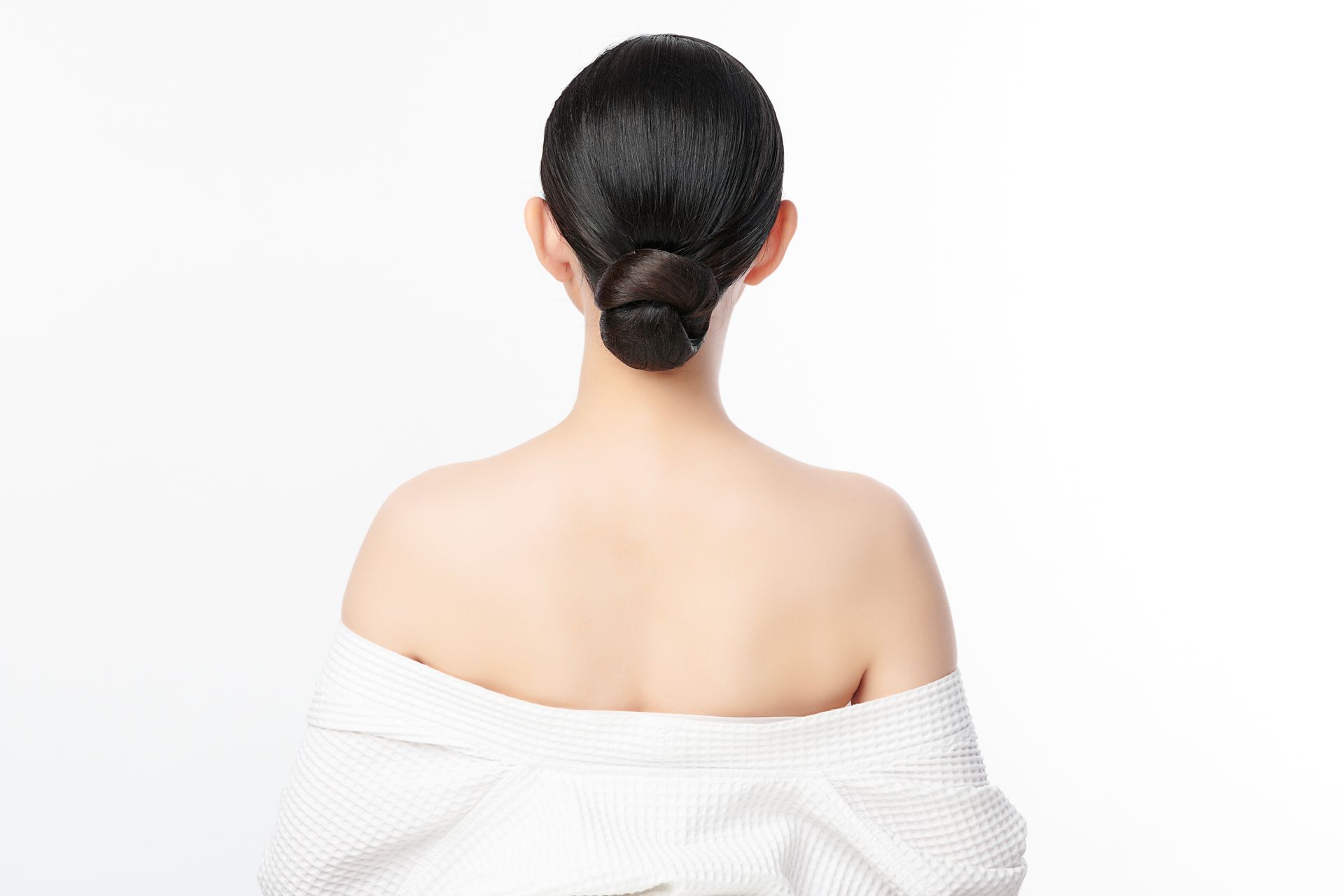 The back of a woman in a white robe with her hair in a bun.