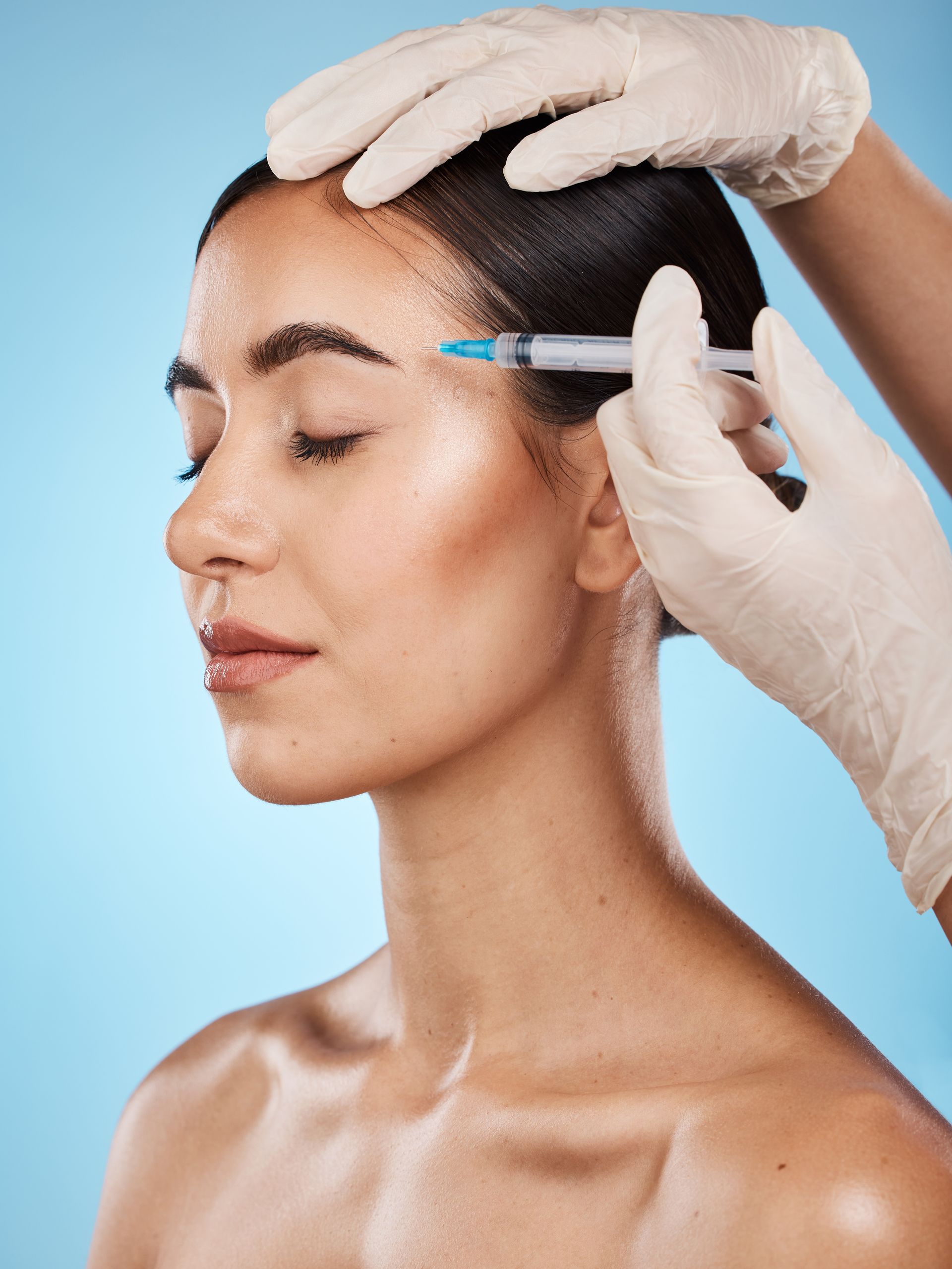 A woman is getting a botox injection in her forehead.